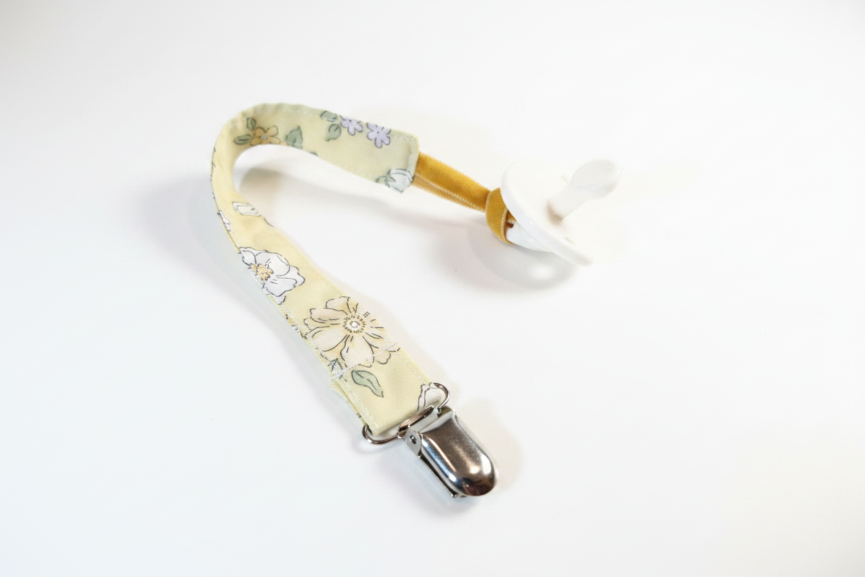Handmade golden yellow floral pacifier clip with silver metal clasp on white studio background