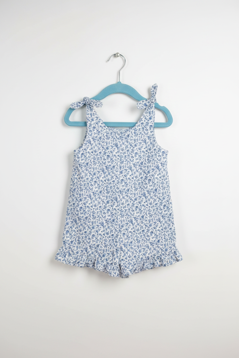 Handmade blue ditsy floral toddler romper with tie straps and ruffle hem on white studio background