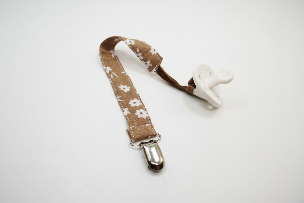 Handmade brown daisy pacifier clip with silver metal clasp on white studio background