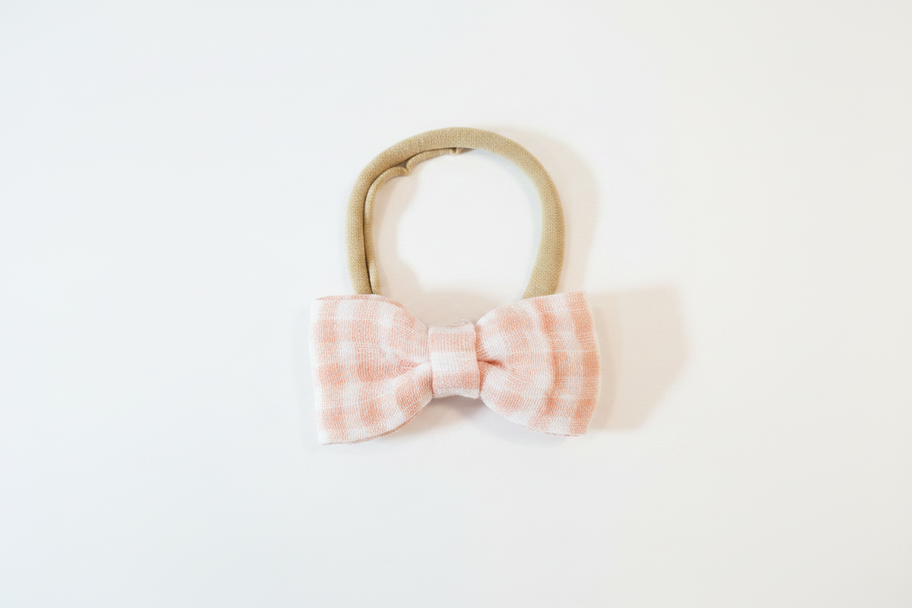 Handmade blush pink gingham bow baby nylon headband laid flat on white studio background