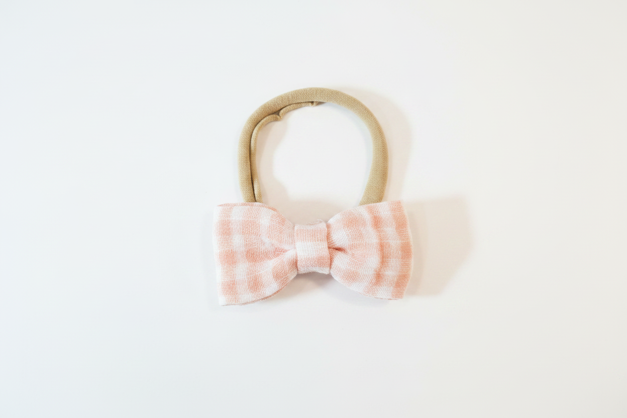 Handmade blush pink gingham bow baby nylon headband laid flat on white studio background