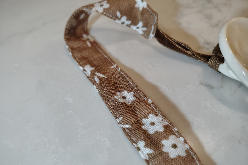 Close-up detail of handmade brown daisy pacifier clip fabric and stitching on white studio background