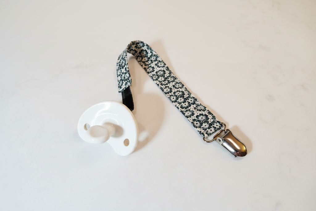 Handmade black and white floral daisy pacifier clip with silver metal clasp on white studio background