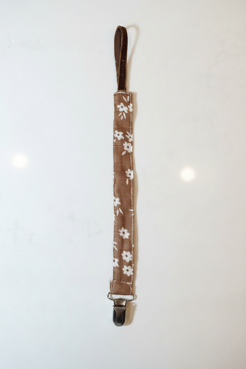 Handmade brown daisy pacifier clip flat lay on white studio background