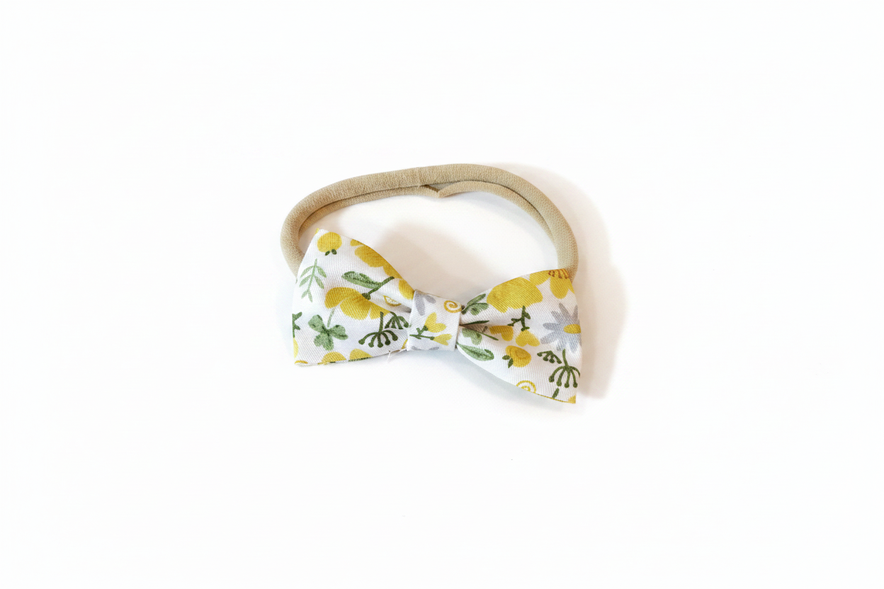 Handmade yellow lemon floral bow baby nylon headband laid flat on white studio background