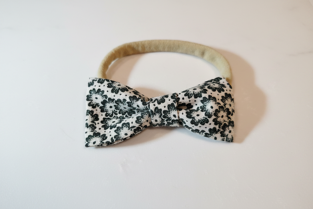 Handmade black ditsy floral bow baby nylon headband laid flat on white studio background