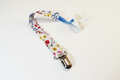 Handmade colorful wildflower pacifier clip with silver metal clasp on white studio background