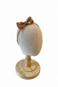 Handmade caramel brown daisy bow baby headband on display stand with white studio background