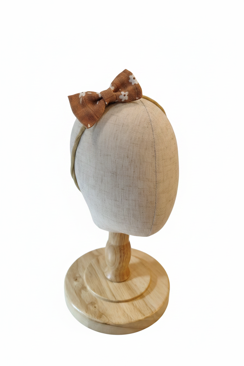 Handmade caramel brown daisy bow baby headband on display stand with white studio background