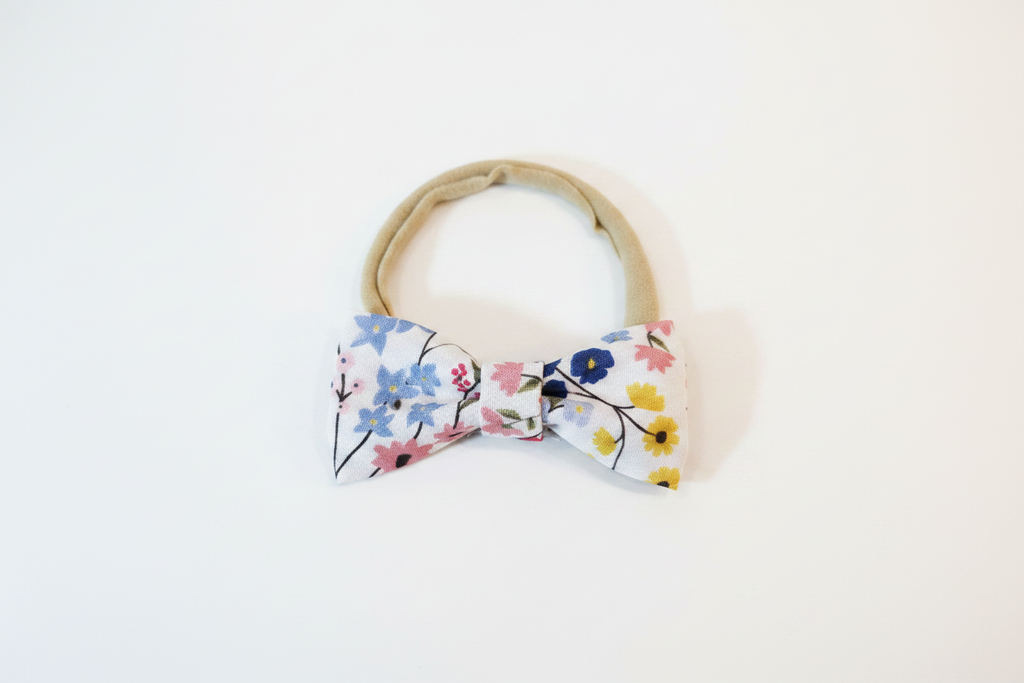 Handmade colorful ditsy floral bow baby nylon headband laid flat on white studio background