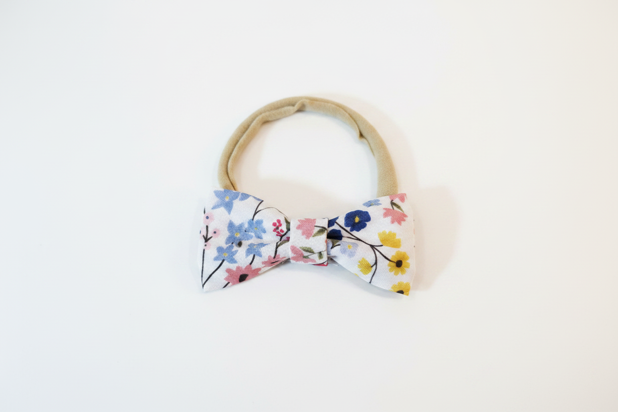 Handmade colorful ditsy floral bow baby nylon headband laid flat on white studio background