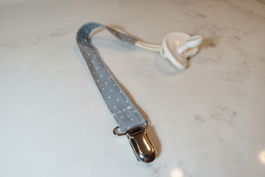 Handmade blue heart pacifier clip with silver metal clasp on white studio background