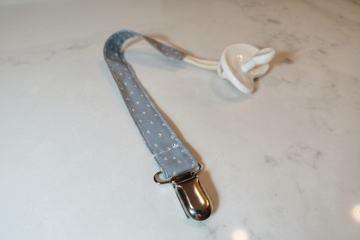 Handmade blue heart pacifier clip with silver metal clasp on white studio background