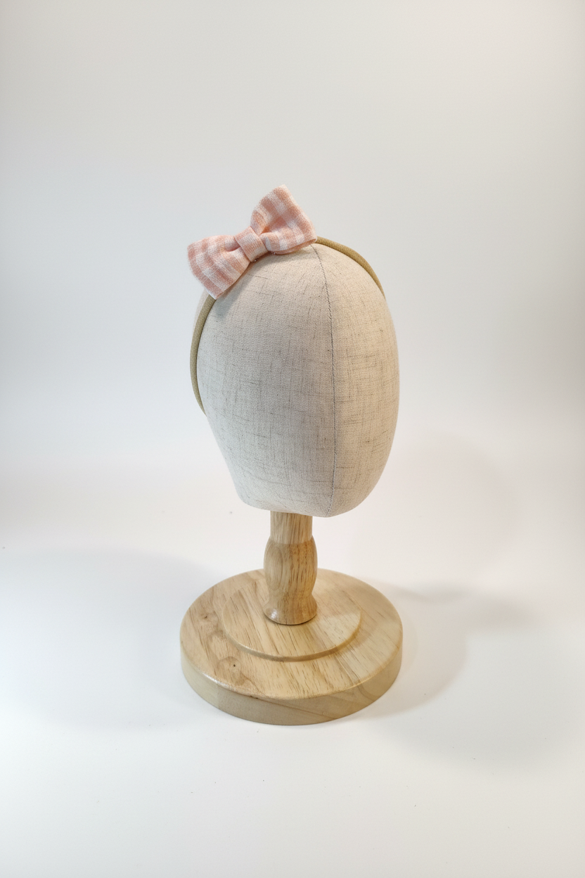 Handmade blush pink gingham bow baby headband on display stand with white studio background