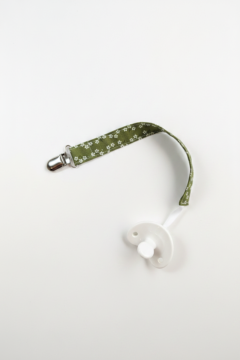 Handmade olive green daisy pacifier clip with silver metal clip and white pacifier on white studio background