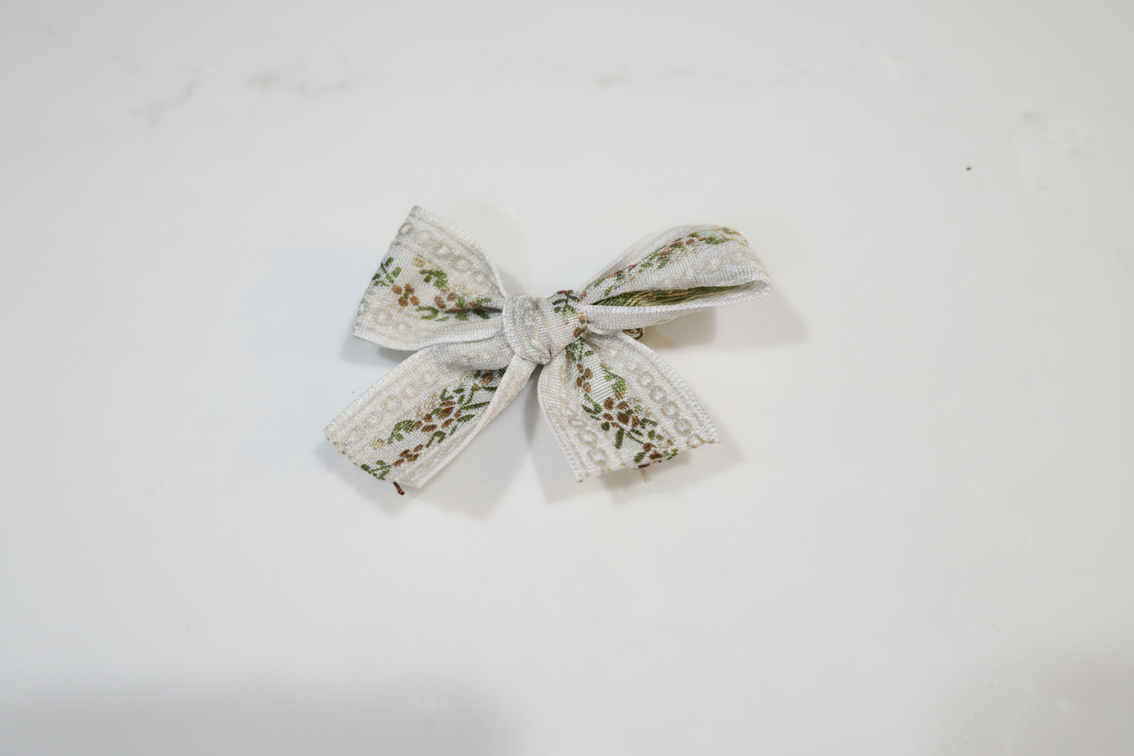 Close-up of single handmade sage vine lace baby hair bow on white studio background