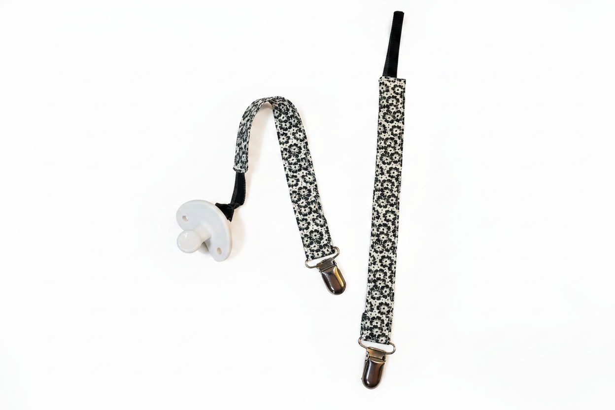 Two handmade black and white floral pacifier clips on white studio background
