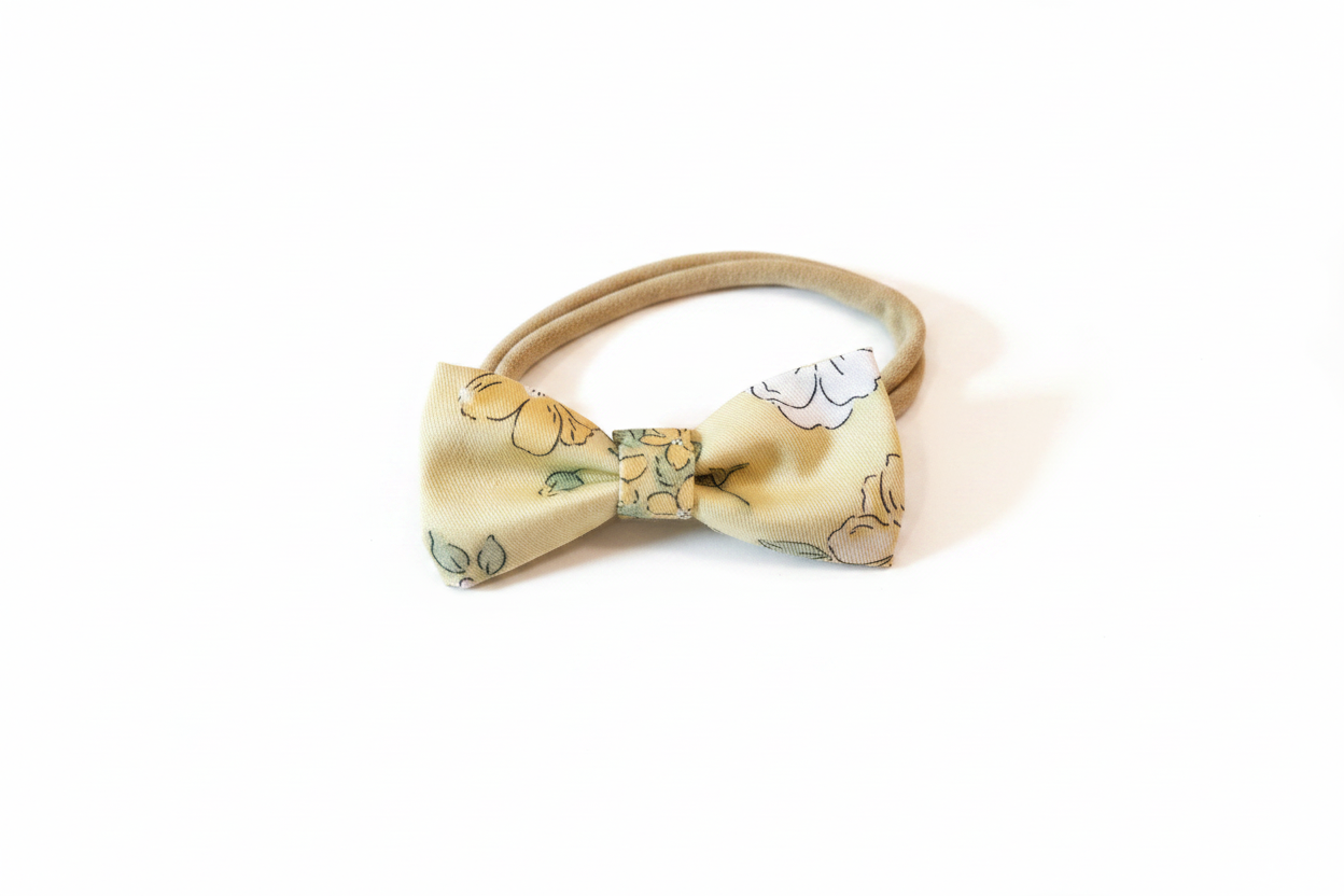 Handmade golden floral bow nylon headband laid flat on white studio background