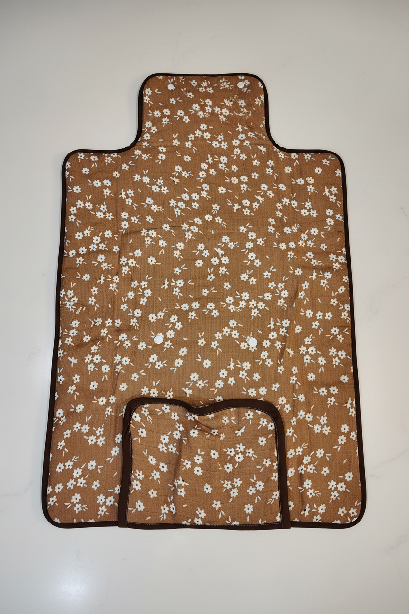 Handmade quilted baby changing mat fully open showing caramel brown daisy print fabric with dark brown trim and gathered pocket on white studio background