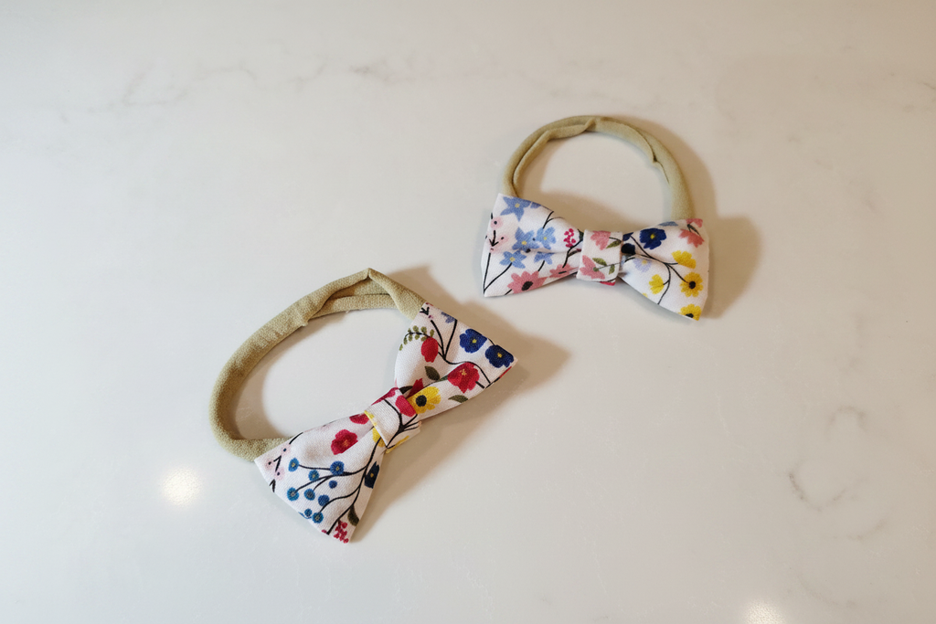 Two sizes of handmade colorful ditsy floral bow baby nylon headbands on white studio background