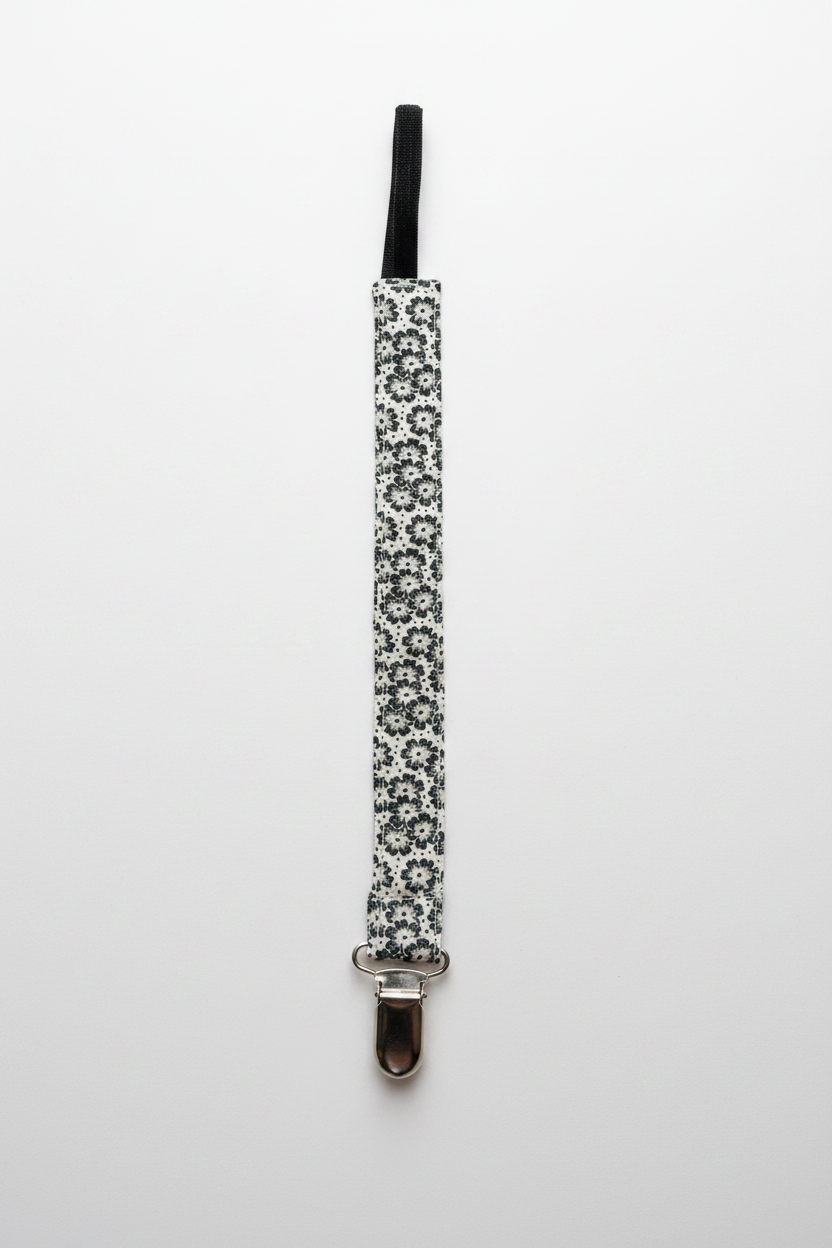 Handmade black and white floral pacifier clip flat lay on white studio background