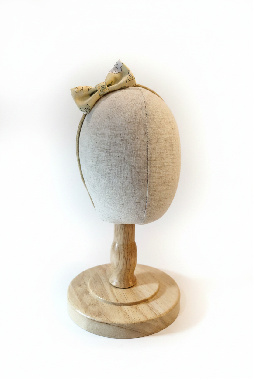 Handmade golden floral bow baby headband on display stand with white studio background