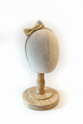 Handmade golden floral bow baby headband on display stand with white studio background