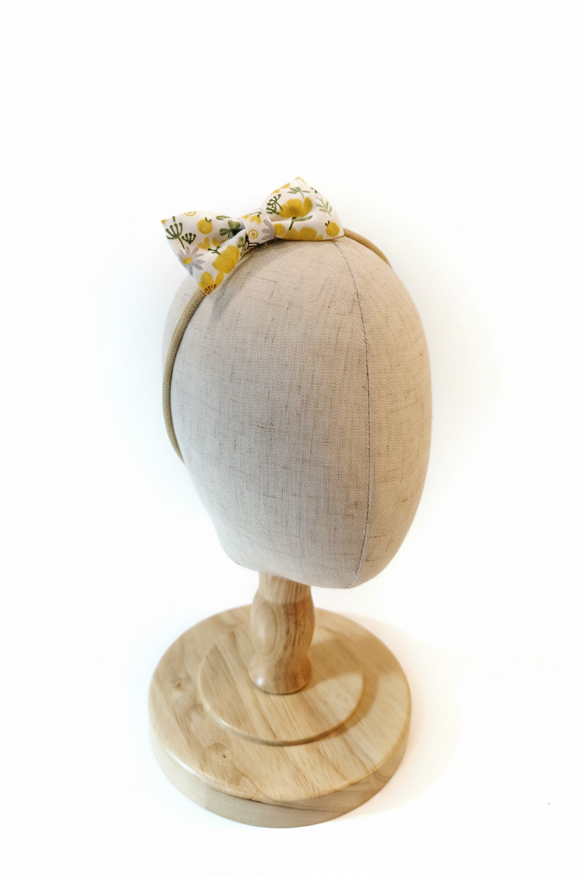 Handmade yellow lemon floral bow baby headband on display stand with white studio background
