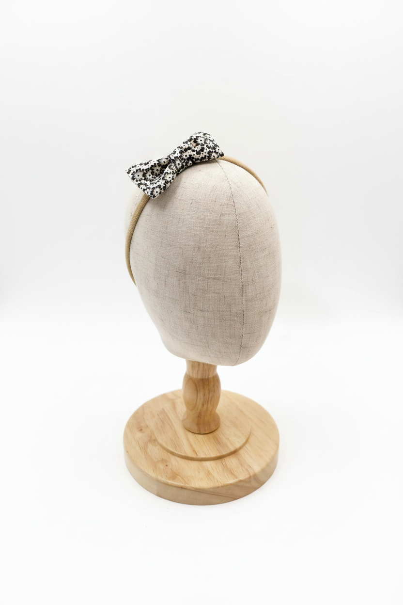 Handmade black ditsy floral bow baby headband on display stand with white studio background