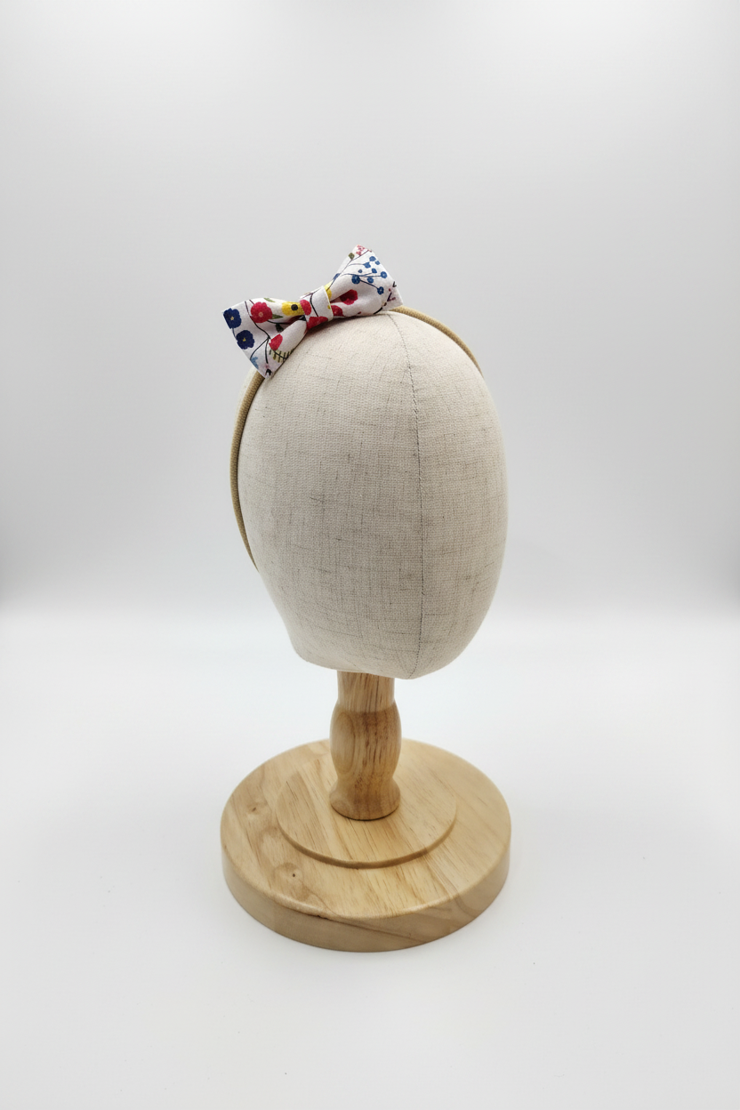 Handmade colorful ditsy floral bow baby headband on display stand with white studio background