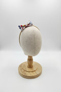 Handmade colorful ditsy floral bow baby headband on display stand with white studio background