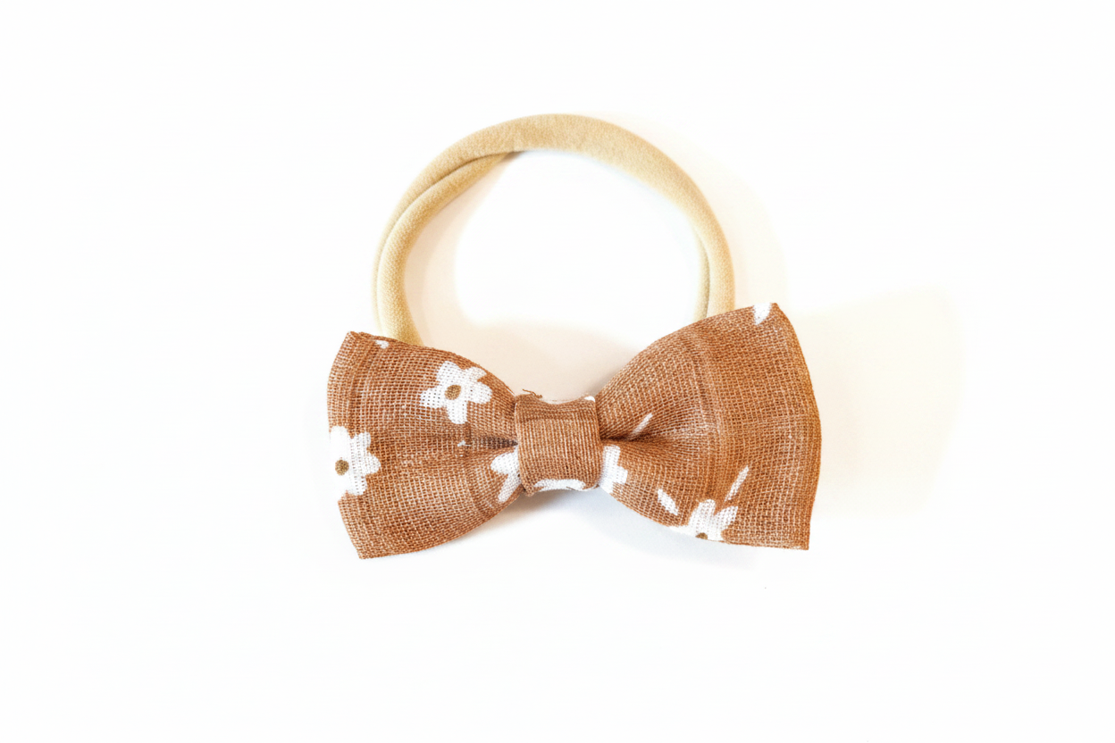 Handmade caramel brown daisy bow baby nylon headband laid flat on white studio background