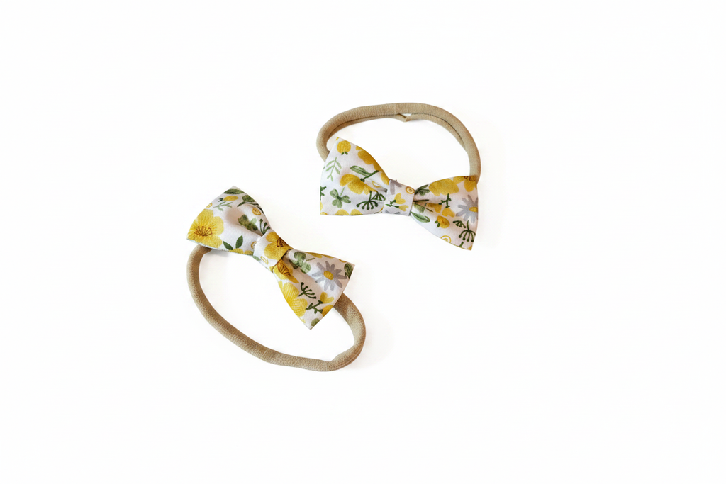 Two sizes of handmade yellow lemon floral bow baby nylon headbands on white studio background