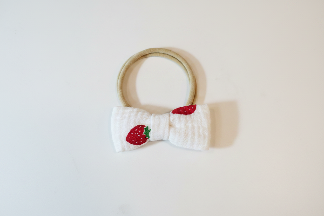 Handmade white textured fabric bow with strawberry appliqué on nylon headband on white studio background