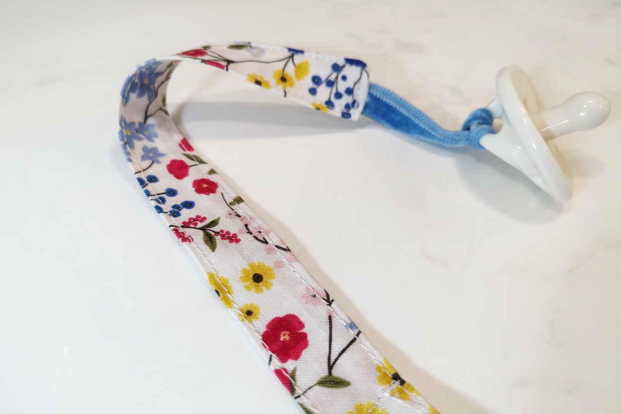 Close-up detail of handmade wildflower pacifier clip fabric and stitching, brightened on white studio background